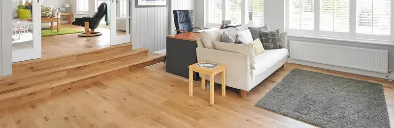 A modern living room with professionally installed laminate flooring, a beige sofa, a small side table, a gray rug, and large windows with white shutters in Marietta, GA